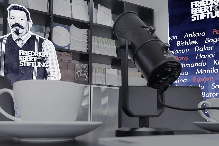 The picture shows a coffee cup in the foreground of a room, alongside a microphone and a cardboard cut-out of Friedrich Ebert.