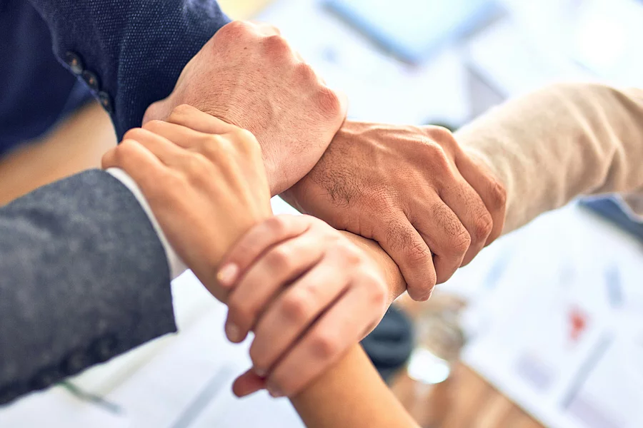 This picture shows the hands of several people clasped together in a gesture of cooperation and trust.