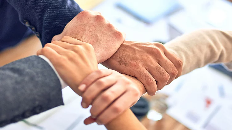 This picture shows the hands of several people clasped together in a gesture of cooperation and trust.